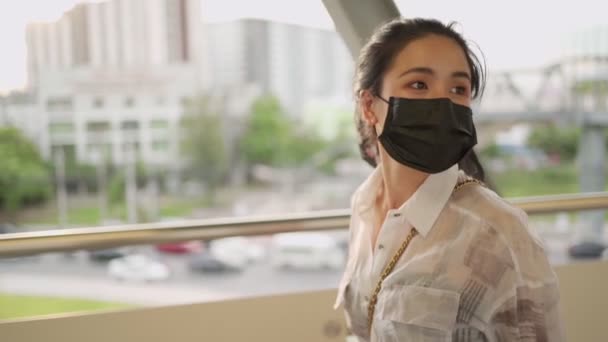 若いアジアの女性は 高架道路を歩いて黒い顔のマスクを着用し 空を歩くCovid 19ウイルスの予防 友人が任命を満たす 公共交通機関での自己保護 黄金の夕日時間 — ストック動画