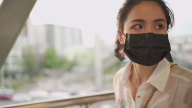 Genç Asyalı bir kadın siyah koruyucu maske takıyor ve metro istasyonunda durup saate bakıyor. Copero-19 'daki bayan arkadaşlarını bekliyor, randevusu var, toplu taşıma aracında kendini koruyor, altın gün batımı.