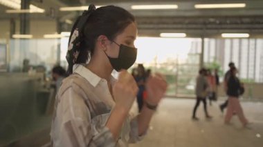 Genç Asyalı kadınlar siyah koruyucu maske takıyor ve metro istasyonunda saatlere bakıyorlar. Covid-19 'daki bayan arkadaşlarını bekliyor, randevusu var, toplu taşımada kendini koruma, altın gün batımı