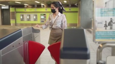Genç Asyalı kadın metro istasyonundaki metro girişinden geçmek için siyah maske takıyor. Kapalı gişe randevusu, karantina karşıtı toplu taşıma, yeni normal yaşam tarzı, dışarı çıkma.