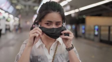 Asyalı kadınlar siyah maske takıyor ve gökyüzü tren istasyonundaki kameraya bakıyor. Kadın metro istasyonundaki kadın, yeni normal yaşam tarzı, kendini koruma, toplu taşıma, akşam beyaz ışığı.