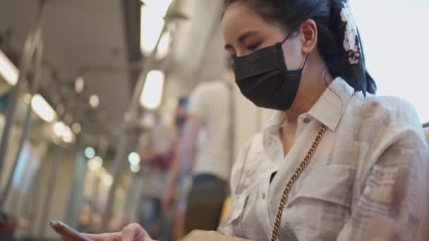 黒い保護マスクのアジアの女性は スマートフォンを使用して地下鉄に座っています コヴィド19の間に家に帰る 新しい普通 地下鉄の女性 公共交通機関の自己保護 社会的な距離の概念 — ストック動画