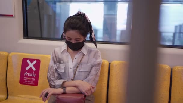 年轻漂亮的亚洲女人 戴着黑色的防护面具 坐在天线阵地铁里 患有眼镜蛇 19型传染病 地铁里的一个女人在她的监视下检查时间 在公共交通工具上自我保护 — 图库视频影像