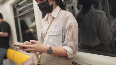 Metroda akıllı telefondan mesaj atan genç Asyalı kadın, covid-19, toplu taşıma iletişimi, sosyal mesafeler, yeni normal ağ bağlantısı 4g 5g kablosuz teknoloji, şehir yaşam tarzı.