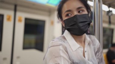 Siyah koruyucu maskeli Asyalı kadın kameraya bakıyor, tren vagonunun, metro istasyonunun merkezindeki direğe tutunun, covid-19, sosyal uzaklık konsepti, yeni normal yaşam tarzı, yavaş hareket 