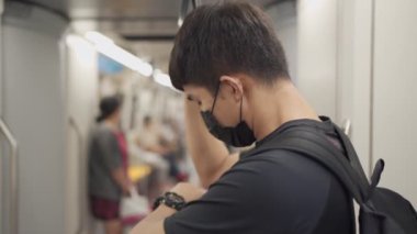 Asyalı adam metro treninde dururken siyah koruyucu maskeyi ayarlıyor, tren yolculuğunda yoğun saatler, yeni normal trafik kazası, toplu taşımada koruma, sosyal mesafeler, bulaşıcı hastalıklar...
