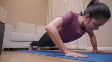 Asyalı genç bir kadın covid-19 sırasında ev egzersizi yapıyor, kadın şınav çekiyor. Kişisel disiplin, spor giyim eğitimi oturma odasında arka planda kanepe ile kadın fitness eğitimi