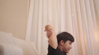 Asyalı genç adam koltuğa yaslanıp kollarını çalıştırıyor. Alternatif halterli halterler, ev egzersizleri, rahat ve plastik su şişeleri uzatma eğitimi alıyor.