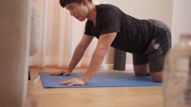 Asyalı genç adam mavi minderde yoga yapıyor, covid-19 kilitlenme sırasında egzersiz yapıyor, ev işi sakin rahatlama, sağlıklı mutluluk, akıllı telefondan ders izleme, yoga esneme ile vücut esnekliği