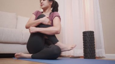 Genç Asyalı bir kadın yoga minderinde bacaklarını açıyor. Oturma odasında kendini kilitliyor, oturma odasında yoga yapıyor, sakin olmak yaşam tarzı, esnek vücut kan dolaşımı.