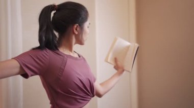 Asyalı genç kadın yoga yaparken kitap okuyor, çoklu görev benlik konsantrasyonu, covid19, ayakta egzersiz, ev yoga egzersizi, sakinlik ve rahatlatıcı yaşam tarzı, sosyal mesafe, sağlık yogası