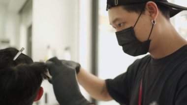 Berber dükkanında erkek saç kesen Asyalı erkek berber siyah koruyucu maske takıyor. Corona virüsü salgını sırasında profesyonel ve berber endüstrisi iş fırsatları.