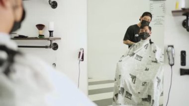 Berber dükkanında saçını kestiren Asyalı adam siyah koruyucu maske takıyor. İş fırsatı Profesyonel Berber. Corona virüsü sırasında insan sağlığı ve berber endüstrisi Codemic Covid-19 yeniden iş kurdu