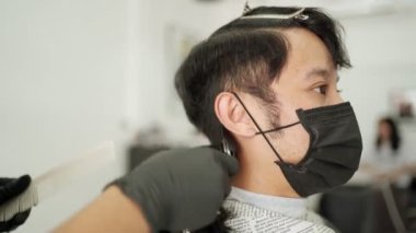 Berber dükkanında saçını kestiren Asyalı adam siyah koruyucu maske takıyor. İş fırsatı Profesyonel Berber. Corona virüsü sırasında insan sağlığı ve berber endüstrisi Codemic Covid-19 yeniden iş kurdu