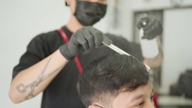 Asyalı erkek berber, siyah maskeli adam saçını kestiriyor. İş fırsatı Barber. Saç spreyi, Corona virüsü Covid-19 sırasında berber işi pandemik anti-karantina sonrası tekrar açıldı