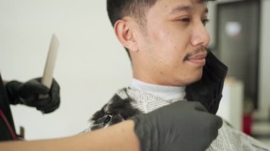 Berber, müşteri maskesini çıkarıp favorilerini kesmek için makas kullanıyor. Berber dükkanından bir saç kesimi al ve siyah koruyucu maske tak. iş fırsatı, Salgın Covid-19 yeniden açılan iş