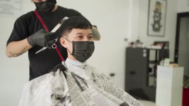 Asyalı adam berber dükkanında saç kestiriyor. Bulaşıcı hastalıklardan korunmak için siyah maske takıyor. Profesyonel berber. erkek sağlığı endüstriyel Corona virüsü Codemic Covid-19 yeniden iş kurdu