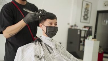 Saç tıraşı olurken koruyucu maske takan Asyalı genç adam bulaşıcı hastalıkları önleme, yeni normal yaşam tarzı. Salgın Covid-19 iş yerini yeniden açtı.