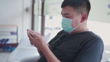 Asyalı adam, Coronavirus salgını sırasında doktorla görüşmek için beklerken cerrahi maske takıyor. Telefon rezervasyonu yapan, kablosuz kolaylık teknolojisi kullanan hasta.  