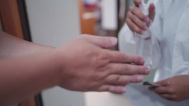 Klinikte dezenfektan kullanan erkek ellerine yardım eden hemşireyi kapat.