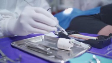 Doktor Dişçi, erkek hasta üzerinde çalışırken tıbbi iğneler batırıyor, diş ameliyatı, sterilize edilmiş tıbbi ekipman çelik tepsisini kapatıyor, dişçilik prosedürünün küçük ayrıntıları, doktor Ppe giysisi giyiyor.
