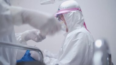 Diş hekimi ve hemşire kadrosu, diş kliniğinde oral ameliyat sırasında bez kaplı yüzü olan hasta üzerinde çalışıyor, Ppe giysi koruyucu maske yüz kalkanı, covid-19 Corona virüs koruması.