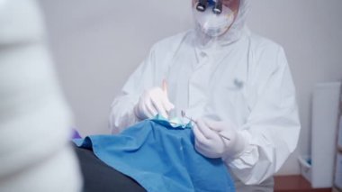 Diş hekimi, hasta üzerinde çalışan, anti-bakteriyel steril ameliyathane, diş kliniğinde oral ameliyat, koruyucu maske yüz kalkanı, covid-19 dezenfekte edilmiş kişisel koruyucu ekipman giyer.