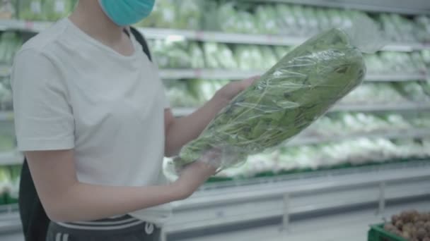 女性はスーパーマーケットで野菜を選択する外科マスク 冷蔵庫棚食料品小売店 食品供給 コロナウイルス パンデミック効果金銭的な生活費 緑色のトーン — ストック動画