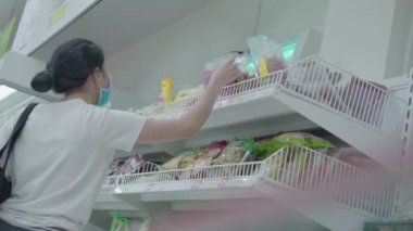 Market covid-19 salgınından mal alırken Asyalı kadın müşteri kendini virüsten koruyor. Koruyucu maskeli bir kadın. Yeni normal bir hayat, alışveriş merkezi süpermarketi, bulanık bir ön plan.