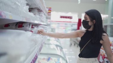 Genç Asyalı bir kadın siyah maske takıyor. Perakende satış mağazalarında ürün seçiyor, insanların mali sorunları, kredi kartı borcu Corona virüsü salgını, satışlarda bütçe yaşayan tüketici alışkanlığı