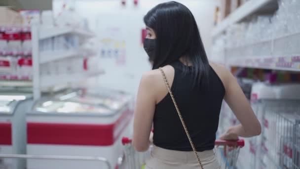 コロナウイルスパンデミックの間 スーパーマーケットで コロナウイルスパンデミック 新しい正常な 予算のウィンドウショッピングで 食料品のプッシュカートで周り回って若いアジアの女性の背後からショット — ストック動画