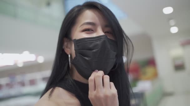 Slow Motion 若い魅力的なアジアの女性の顔のマスクの下の笑顔 コロナウイルスパンデミックの間に食料品のスーパーマーケットの店の中を歩いている間 隔離は距離を保ちます カメラを見るモデル — ストック動画