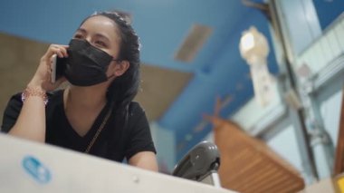 Siyah koruyucu maskeli genç Asyalı kadın havaalanında telefon ediyor. Trolley arabası, Corona virüsü salgını, covid-19 salgını, yeni normal sosyal uzaklık, alması için birini ara, teknoloji... 