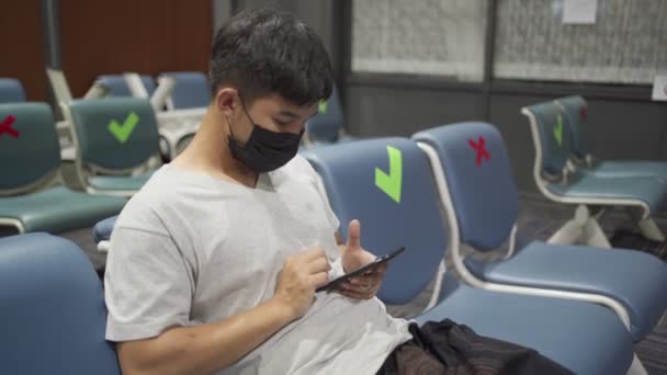 アジアの男性は ソーシャル距離のコンセプトチェアにスライド電話を座って黒いマスクを着用し 距離間隔を保ちます 新しい通常のルーチンCovid 19パンデミック 公共無線Lanインターネット 携帯電話キャリア — ストック動画