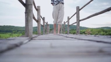 Genç bir kadın tahta köprüde yalınayak yürüyor, sakin sakin bir düşünce, rahat bir yürüyüş yolu, doğada hayat, alçak açılı bir manzara, kırsal alanda güzel bir yürüyüş. 