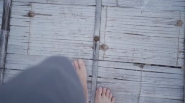 Genç kadın yalınayak yavaşça tahta köprüde yürüyor, sakin sakin hareketler, arka planda dağ ve ağaçlar, kutunun dışına adım at, doğada rahatlama, alçak açı kamerası.