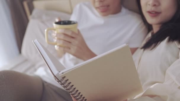 アジアのレズビアンガールフレンドが一緒に朝の時間を読んで ベッドでコーヒーを飲みます Lgbt同性愛者の平等幸福のライフスタイルの関係 暖かい居心地の良い快適な寝室 — ストック動画