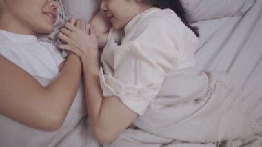 Asyalı genç lezbiyen çift yatağa uzanıyor, el ele tutuşup öpüşüyorlar, LGBTQI gururu, bağ kurma ilişkisi, rahat yatak odası ve sıcak battaniye, cinsel eşitlik mutluluk yaşam tarzı