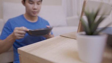 Genç Asyalı adam tabletten komedi programını izlerken eğleniyor. Evin içinde basit bir yaşam tarzı var. Tek başına yemek yiyor, kanepeye oturuyor, aç bir şekilde yemek yiyor ve gülüyor.