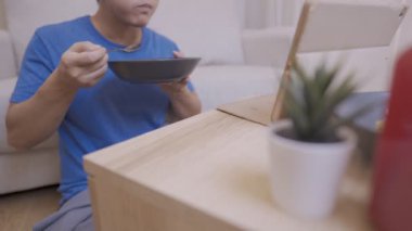 Genç Asyalı adam tabletten komedi programını izlerken eğleniyor. Evin içinde basit bir yaşam tarzı var. Tek başına yemek yiyor, kanepeye oturuyor, aç bir şekilde yemek yiyor ve gülüyor.