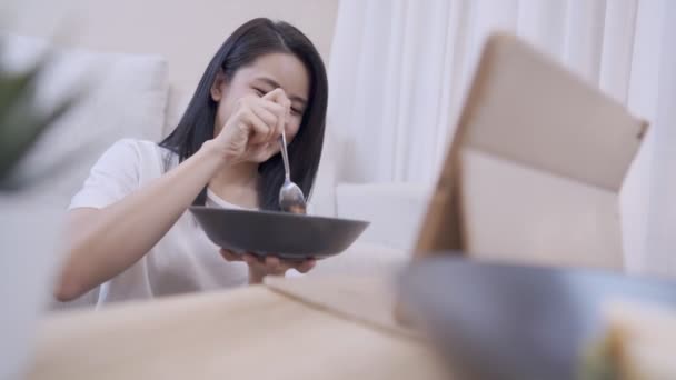 年轻的亚洲女人一边吃着晚餐 一边看着网上的内容开心地笑着 坐在地板上 沙发在客厅里 简单而健康地生活着 独自呆在家里 — 图库视频影像