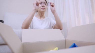 Genç Asyalı bir kadın küçük bir karton kutu paketi açıyor, kadın alıcılar kutuları boşaltıyor, erzak teslimatı, yeni bir daireye taşınma, yeni bir yere depolama alanı.