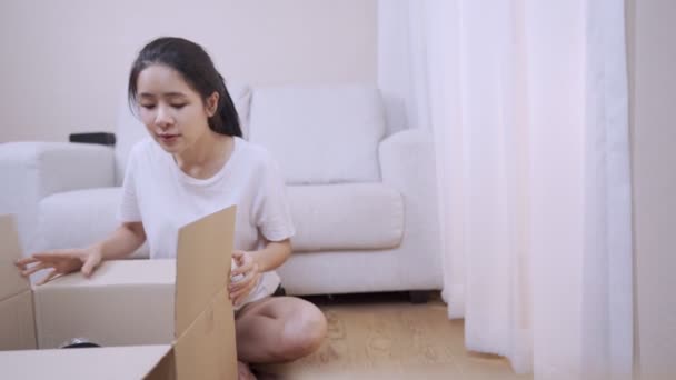 アジアの若いアジアの女性アンパックカートン小包ボックス 古いものを整理して見て リビングルームに座って 良い古い思い出 新しいアパートに移動する移転 フロントビュー — ストック動画