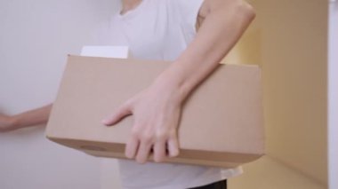 Genç Asyalı kadın yeni evin ön kapısına giriyor, elinde karton kutu, yeni bir daireye taşınıyor. Yerleştirme ve ipotek yeni bir dairede taşınıyor, karton kutuları yeni odaya taşıyor.