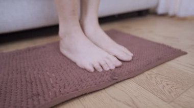 Yakın görüş genç bayan yalın ayak kanepeden kahverengi zemin paspasına adım ev oturma odası, alt vücut parçası, ev temizliği, ev dekorasyonu ahşap döşeme. 