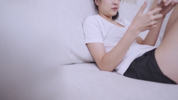 アジアの若い女性は 快適なソファーでリラックス オンラインソーシャルメディア モバイルアプリケーション 個人的なスペース ソファー ホームリビングルームで快適に膝で交差した — ストック動画