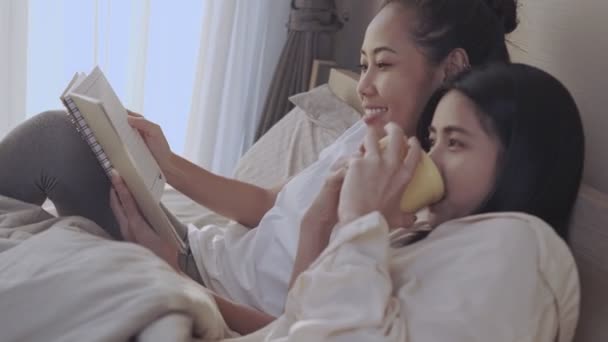 アジアのレズビアンガールフレンドが一緒に朝の時間を読んで ベッドでコーヒーを飲みます Lgbt同性愛者の平等幸福のライフスタイルの関係 暖かい居心地の良い快適な寝室 — ストック動画