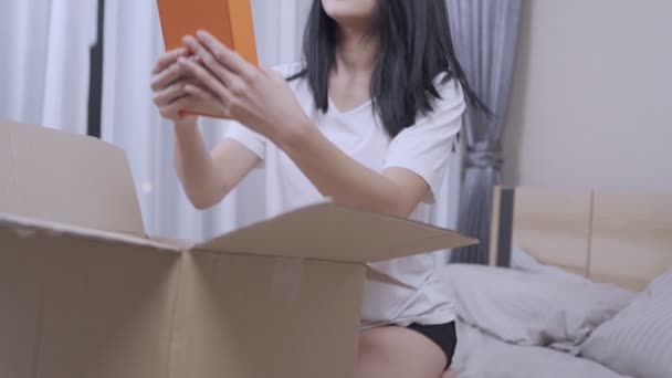 願わくば興奮する若いアジアの女性は 受信したものをオンライン注文からチェックし ボックスを解除する郵便配送小包は 注文または配達段ボール箱 移動家 インターネットショッピングに満足します — ストック動画