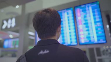 Asyalı genç erkek yolcu havaalanı uçuş saatine bakıyor, uçak bileti rezervasyonu, yeni normal yolcu, Boş havaalanı terminalinde, maske koruması, Corona virüsü kovid19 