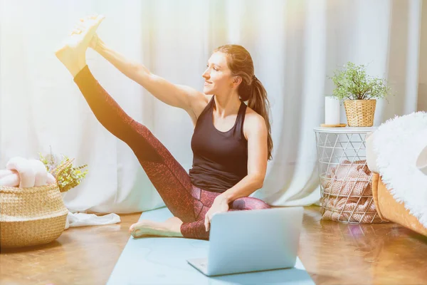Young attractive sporty woman practicing yoga. Trains to sit on the twine and stretching, working out at home in living room. Sport and recreation concept.